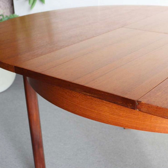 Mid-century British vintage teak dining table with smooth wood grain and round, tapered legs from Denmark.