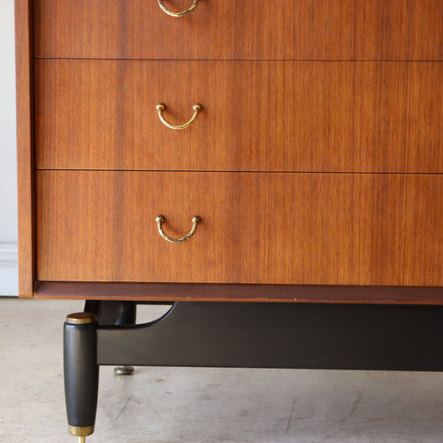 Vintage G-Plan mid-century teak chest with brass handles, black tapered legs, and visible wood grain detailing.