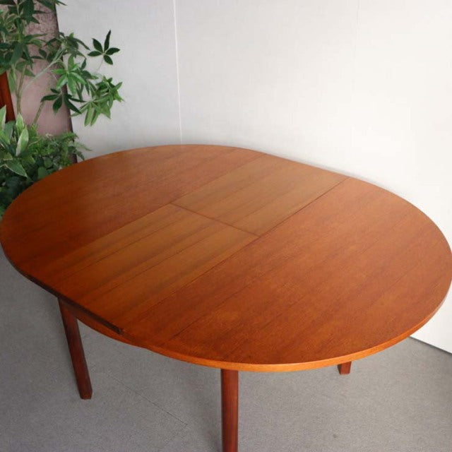 Vintage mid-century British teak dining table with oval top and smooth wood grain, slender legs.