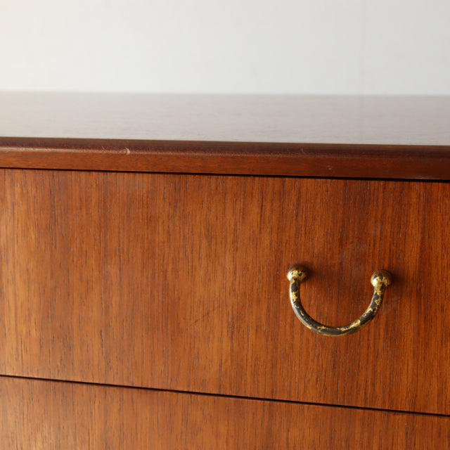 Mid-century British G-Plan chest in vintage teak featuring smooth wood grain and brass handle on sleek drawer.