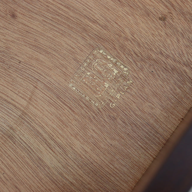 Close-up of vintage G-Plan teak wood surface with British mid-century Denmark label and visible wood grain.