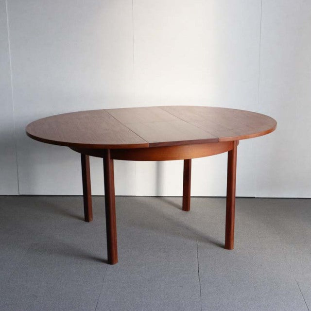 Oval mid-century vintage teak dining table with smooth wood grain and slender tapered legs, British design influence.