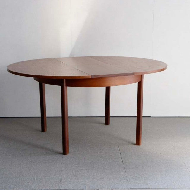 Vintage mid-century teak dining table with oval top, smooth wood grain, and slender round legs, British-Denmark style.