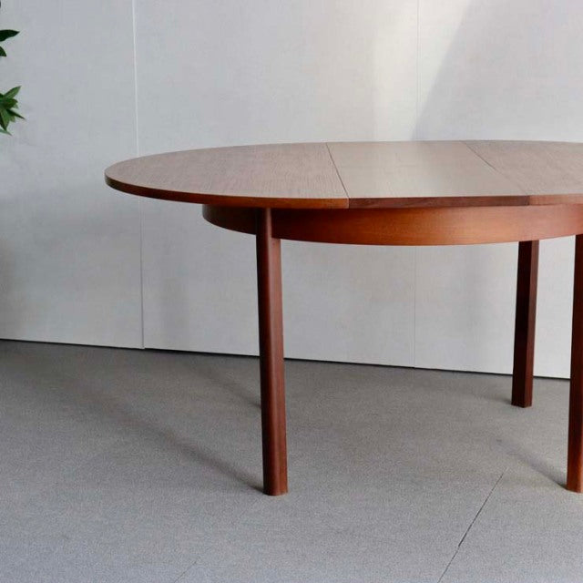 Mid-century British vintage teak dining table with oval top, smooth wood grain, and slender round legs in Danish style.