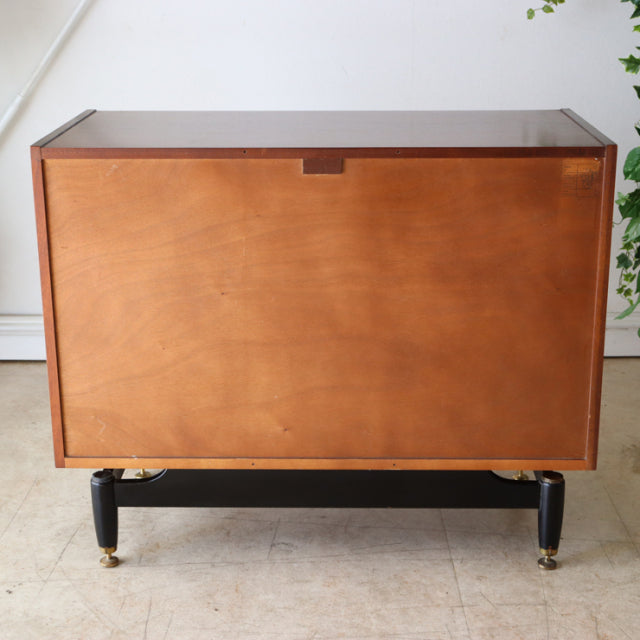 Vintage British mid-century G-plan chest in teak with smooth wood grain, black tapered legs, and brass feet.