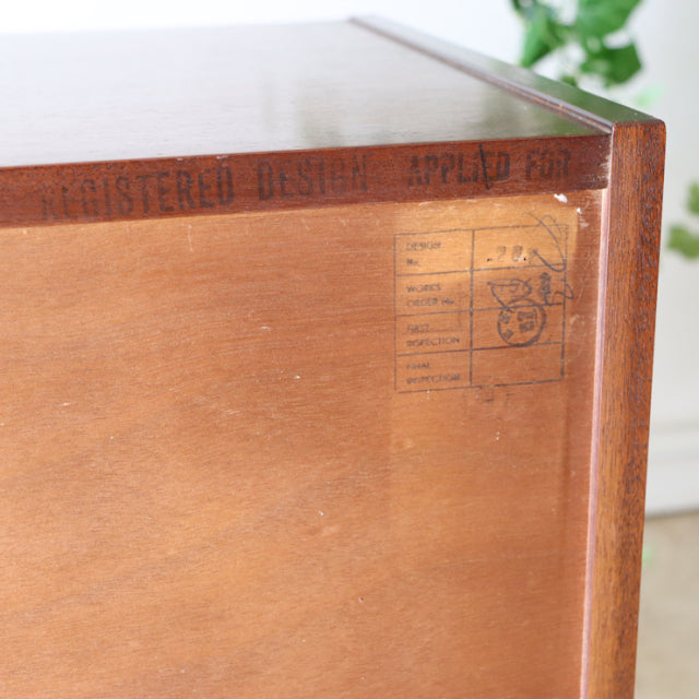 Close-up of vintage G-plan teak chest corner showing wood grain, stamped British mid-century Denmark design marks, and clean .