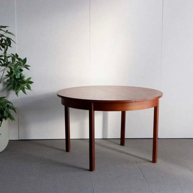 Vintage mid-century teak dining table with round top, sturdy tapered legs, and smooth wood grain from British-Denmark design.