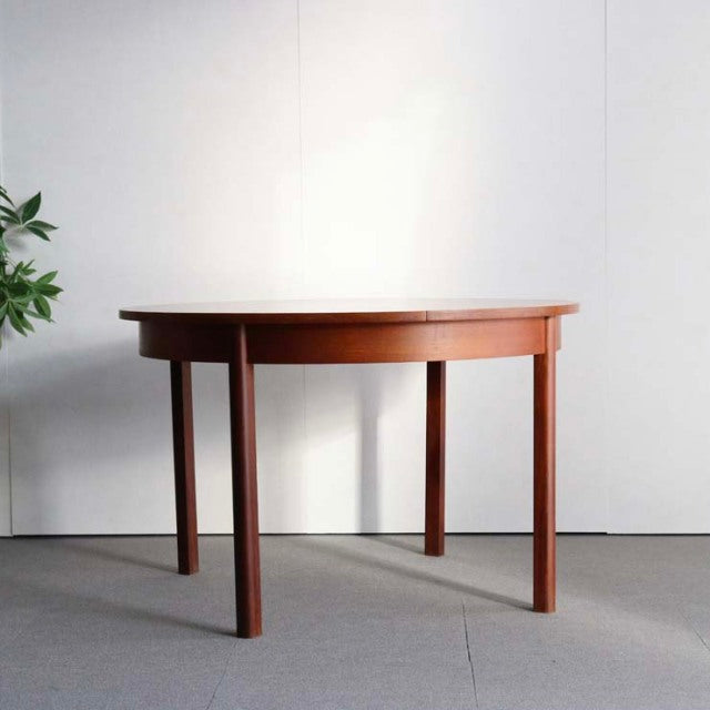 Mid-century British vintage teak dining table with round top and four slender tapered legs, showcasing rich wood grain and.