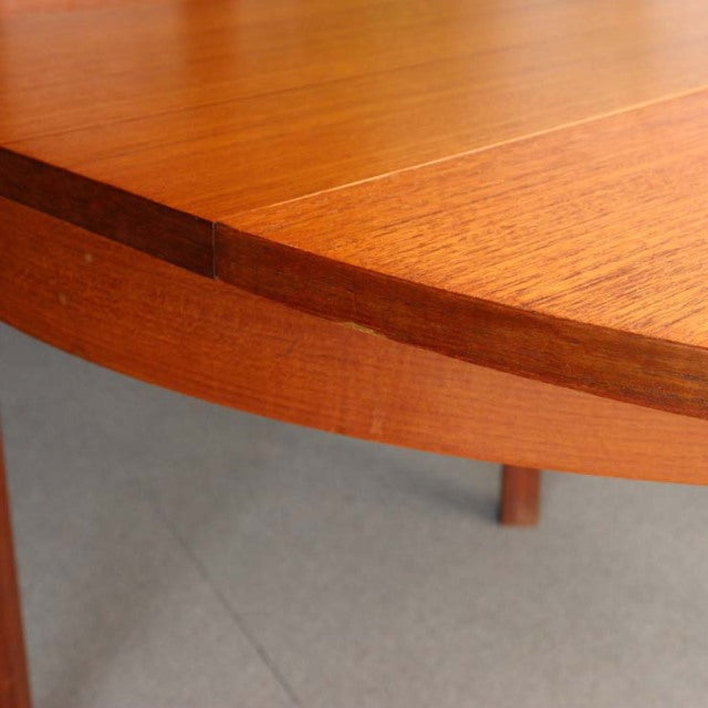 Vintage British mid-century teak dining table with smooth wood grain and rounded edges, open extension mechanism visible.