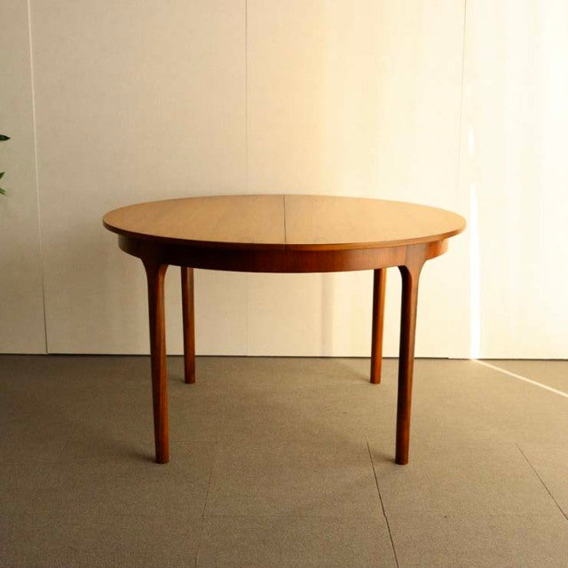 Mid-century British vintage teak round dining table by McIntosh with slender tapered legs and smooth wood grain.