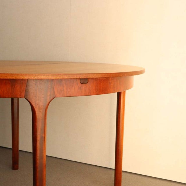 Vintage British mid-century teak round dining table with smooth grain and slender tapered legs.