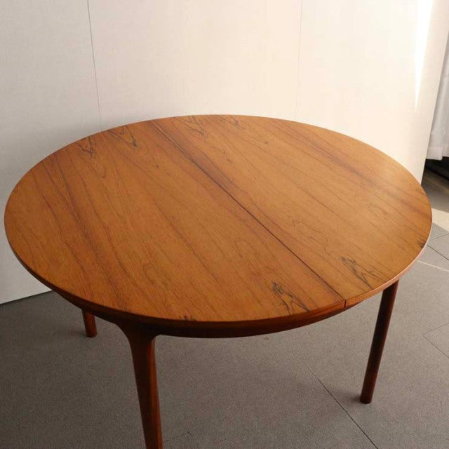 Vintage mid-century teak round dining table by British brand McIntosh, showcasing smooth wood grain and slender tapered legs.