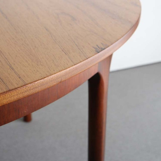 Round vintage teak dining table with smooth wood grain, slender tapered legs, mid-century British-Denmark design.