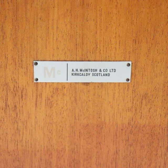 Close-up of vintage teak wood grain with rectangular metal brand plate reading A.H.