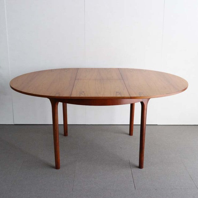 Mid-century British vintage teak round dining table with smooth wood grain and slender tapered legs.