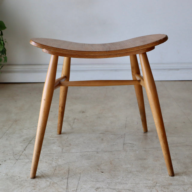 Vintage mid-century British ERCOL butterfly stool in warm teak with smooth curved seat and tapered legs showing fine wood.