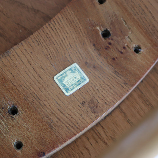 Close-up of vintage teak wood grain on British mid-century Ercol Butterfly Stool seat, showing original label and screw holes.