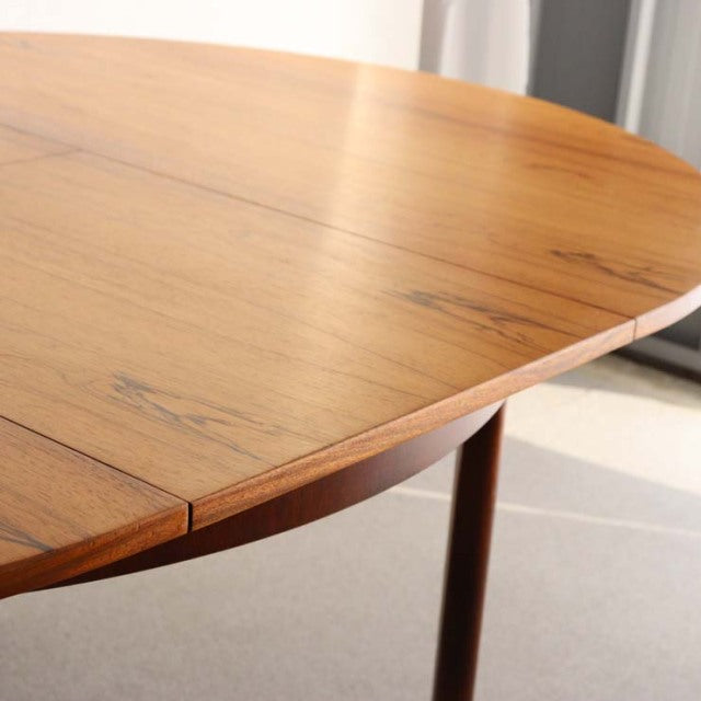 Vintage British mid-century teak round dining table with smooth wood grain and slender tapered legs.