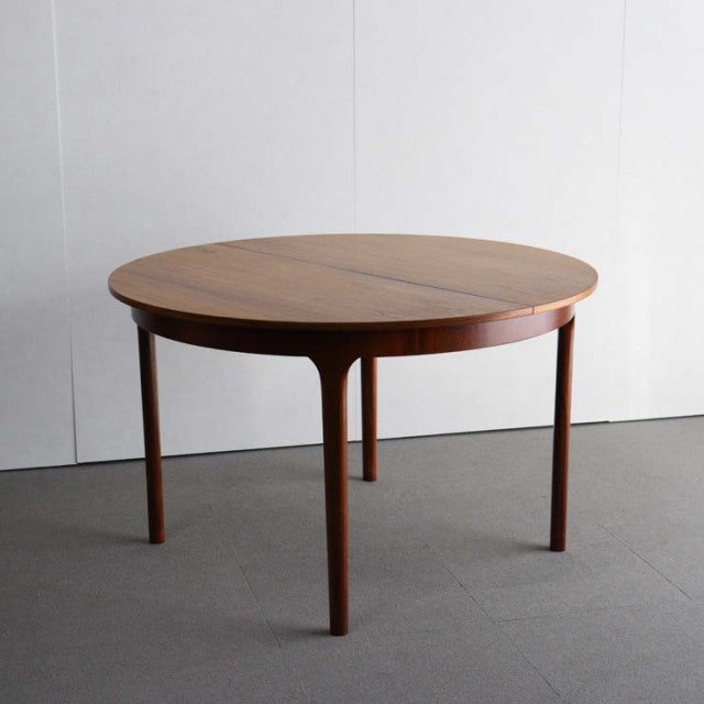 Vintage mid-century British teak round dining table with smooth wood grain and slender tapered legs.
