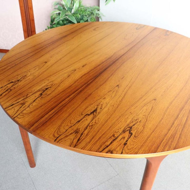 Vintage mid-century British teak round dining table with smooth wood grain and slender tapered legs, elegantly crafted in.