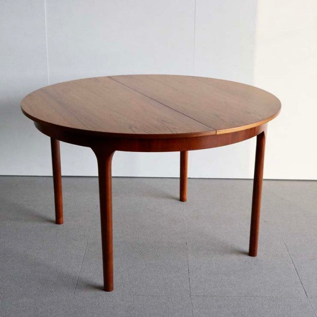 Vintage teak round dining table with smooth wood grain, slender tapered legs, mid-century British design inspired by Denmark.
