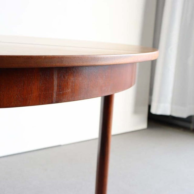 Vintage British mid-century teak round dining table with smooth wood grain and slender tapered leg, classic Denmark design.