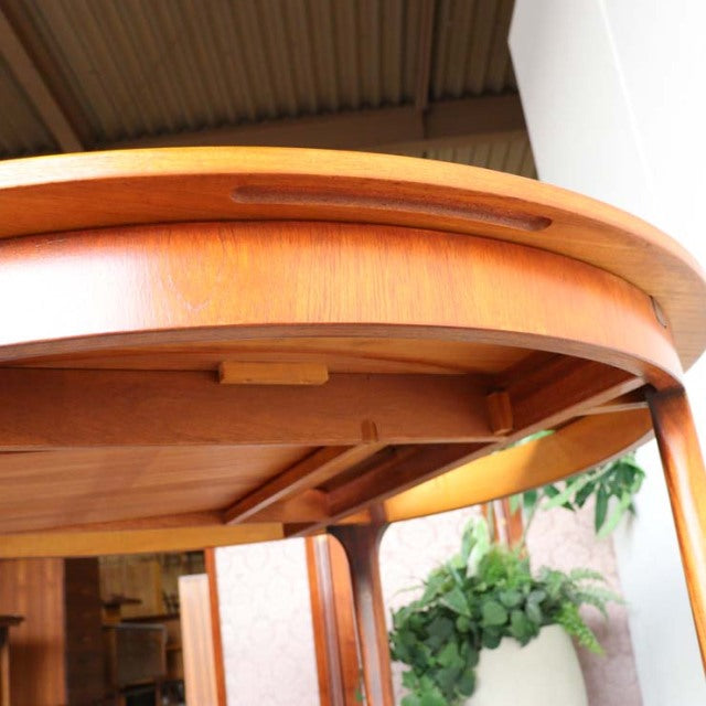 Vintage teak round dining table with smooth wood grain, mid-century British design, solid curved legs, and clear varnish.