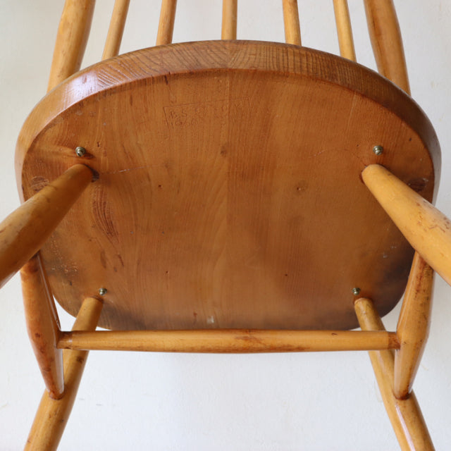 Vintage British mid-century Ercol dining chair in natural teak with visible wood grain and spindle legs viewed from below.