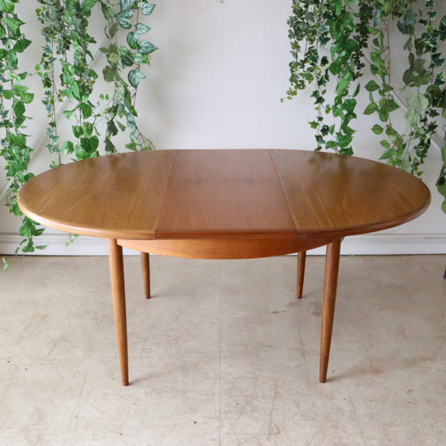 Vintage G-Plan teak dining table with oval top, mid-century British design, slender tapered legs, warm wood grain finish.