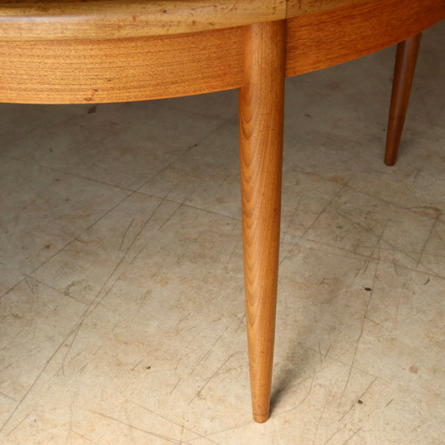 Mid-century British G-Plan vintage teak dining table leg with smooth wood grain and tapered design on light floor.