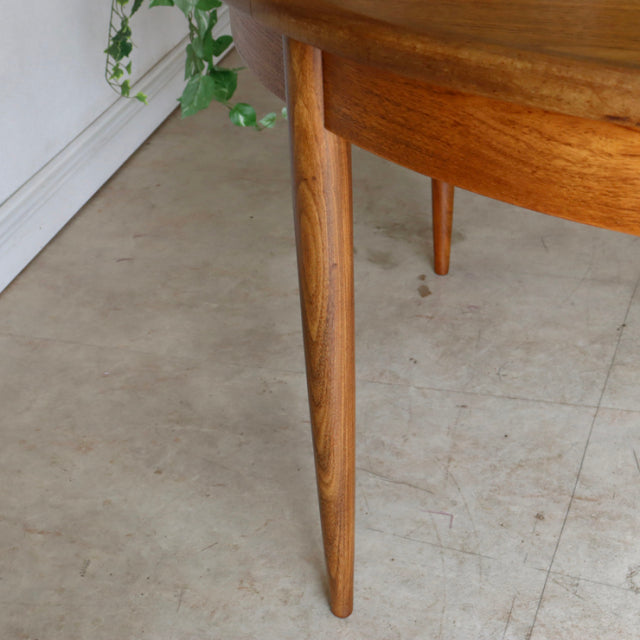 Mid-century British G-Plan teak dining table with smooth oval surface and tapered round legs showing rich wood grain.