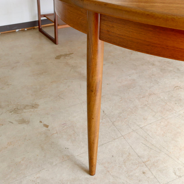 Mid-century British G-Plan teak dining table leg with smooth wood grain and tapered rounded design against a neutral floor.