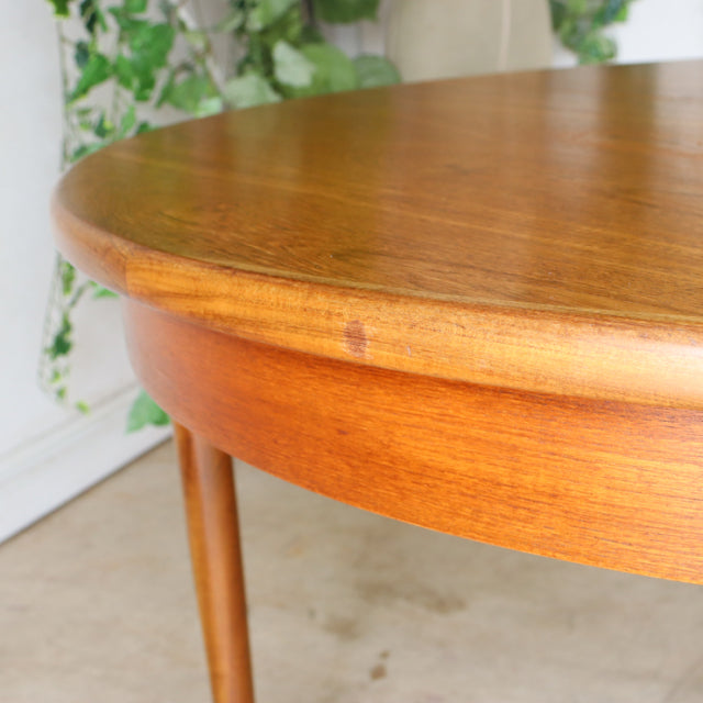 Round vintage mid-century teak dining table by British G-Plan with smooth wood grain and slender tapered legs.