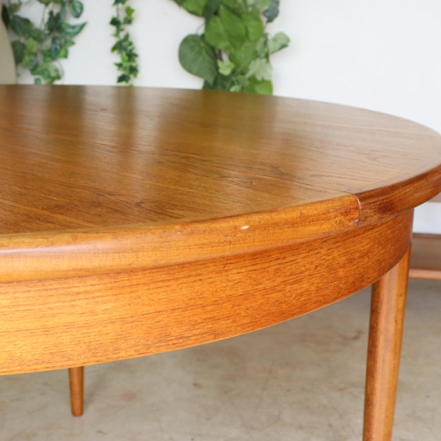 Vintage British mid-century teak G-Plan dining table with smooth round top, visible wood grain, and tapered legs.