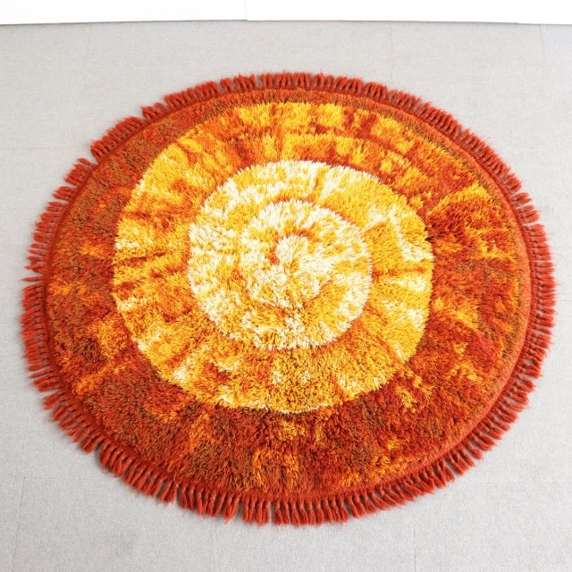 Round vintage mid-century rug with vibrant orange, yellow, and red spiral pattern and fringed edge.
