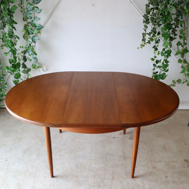 Vintage mid-century British G-Plan teak dining table with smooth oval top and tapered legs in warm wood grain.
