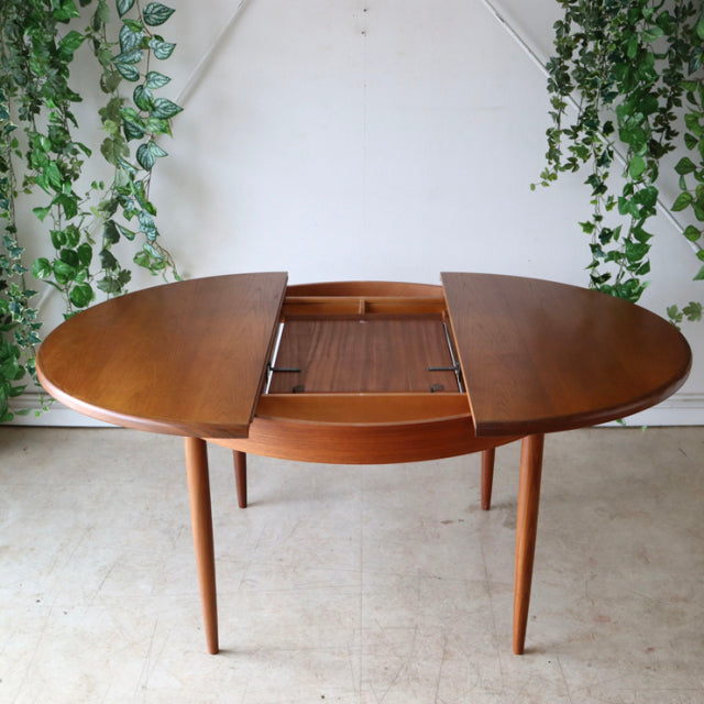 Vintage British G-plan round teak dining table with mid-century tapered legs and extendable top showing wood grain.