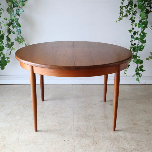 Vintage G-Plan round teak dining table with visible wood grain, tapered mid-century British legs, Danish design influence.