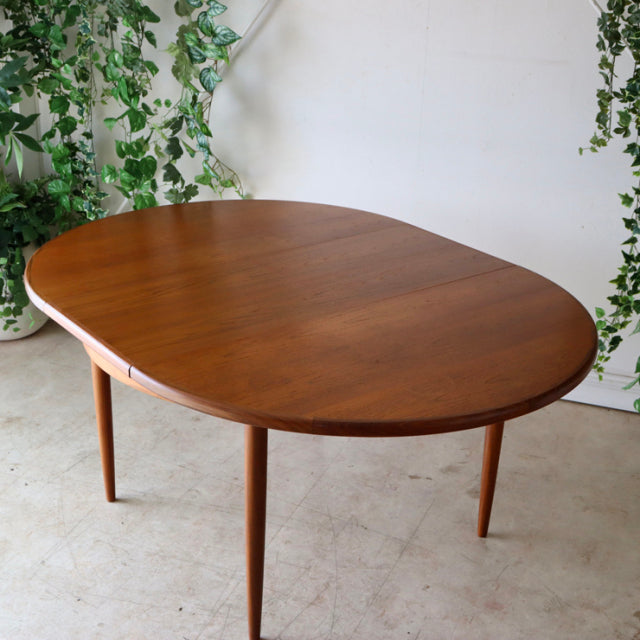 Vintage teak G-Plan round dining table with smooth wood grain and slender tapered legs, showcasing mid-century British.