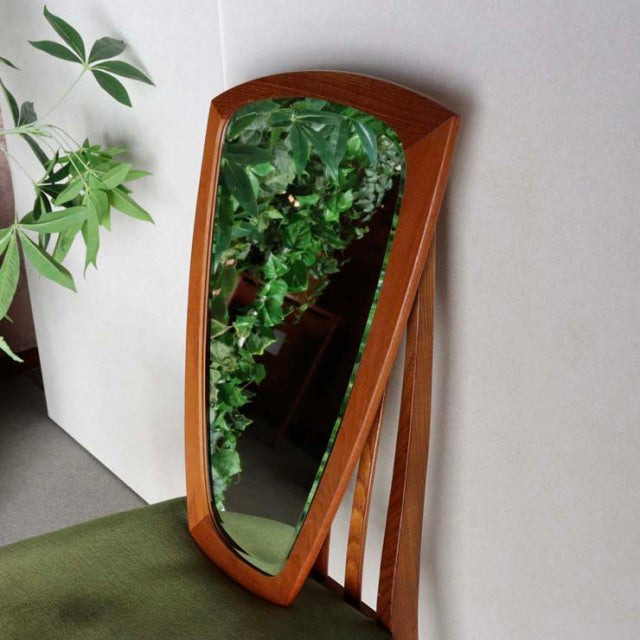 Mid-century vintage teak wall mirror from Denmark with curved organic shape and rich wood grain detail, leaning on a beige.
