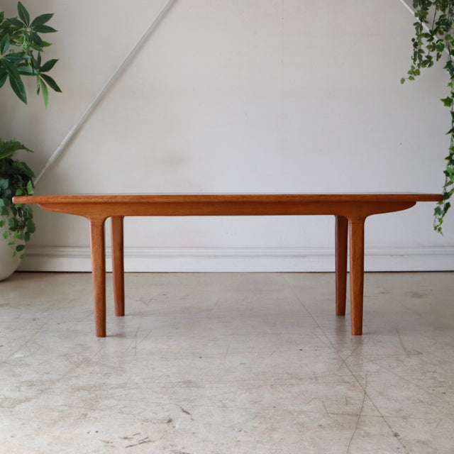 Mid-century vintage teak coffee table with smooth wood grain, slender round legs, British-Denmark design influences.