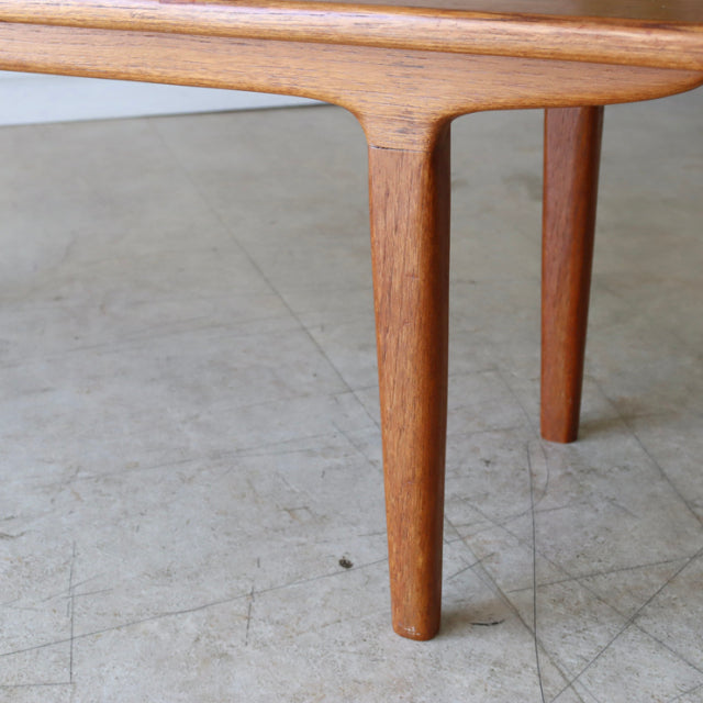 Mid-century British teak coffee table leg with smooth rounded edges and visible wood grain on concrete floor.