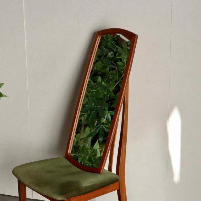Mid-century British vintage teak full-length mirror with rich wood grain and slender frame, leaning on green velvet seat.