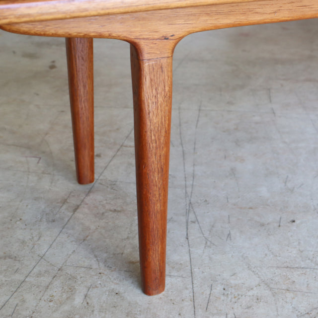 Mid-century British vintage teak coffee table corner showing smooth wood grain and tapered round legs on concrete floor.