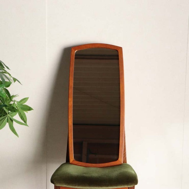 Mid-century British vintage teak mirror with tall, rectangular curved frame and green velvet cushioned base.