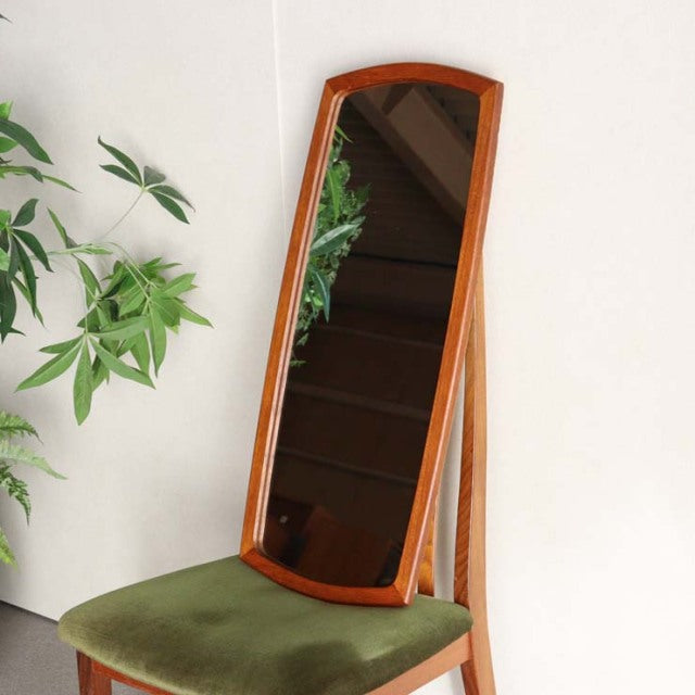 Mid-century British vintage teak mirror with slender rectangular frame, smooth wood grain, and angled stand, resting on.