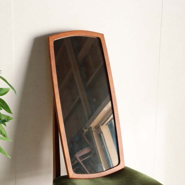 Mid-century British vintage teak mirror with curved rectangular frame and warm wood grain, leaning against white wall.