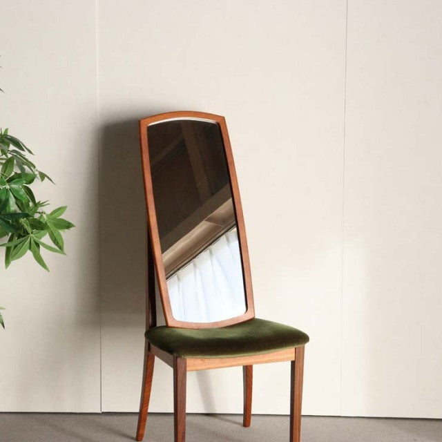 Mid-century British vintage teak mirror with slim, curved frame and warm wood grain, standing on four slender legs above.