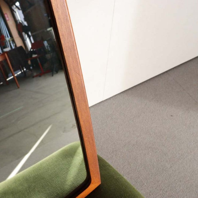 Mid-century British vintage teak mirror with slim rectangular frame and visible wood grain finish, resting against a green.