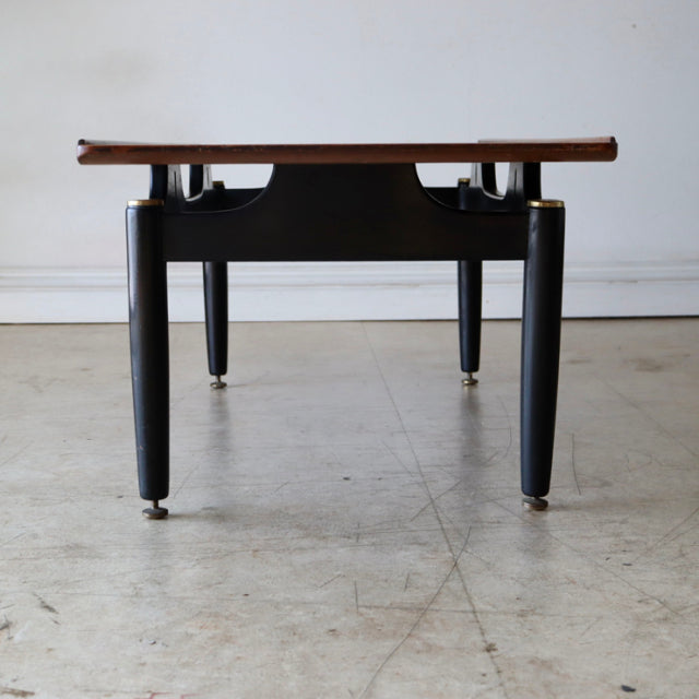 Mid-century British G-Plan teak coffee table with black tapered legs, brass-capped feet, and visible wood grain top.